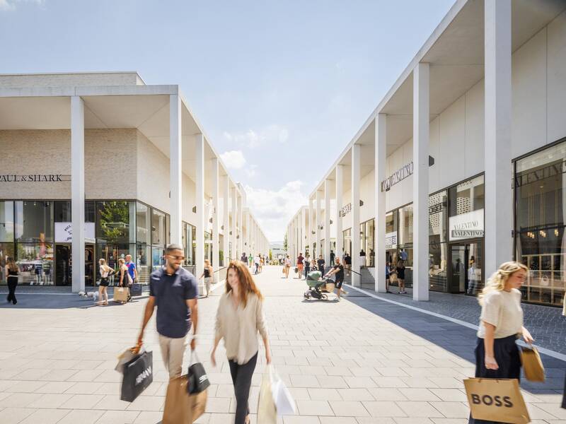 Eine Einkaufsstraße mit modernen Gebäuden und Menschen, die Einkaufstüten tragen.