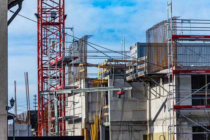Nähere Aufnahme eines Hausbaus. Die Außenmauern sind teilweise mit einem Gerüst versehen. Im linken Bildbereich befindet sich der Mast eines roten Krans. Nähere Aufnahme eines Hausbaus. Die Außenmauern sind teilweise mit einem Gerüst versehen. Im linken Bildbereich befindet sich der Mast eines roten Krans.