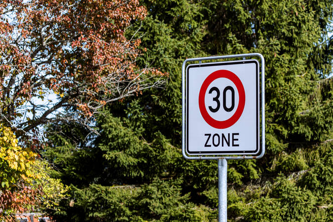Ein Verkehrsschild, das auf den Beginn einer Tempo-30-Zone hinweist. Im Hintergrund steht eine grüne Tanne. Ein Verkehrsschild, das auf den Beginn einer Tempo-30-Zone hinweist. Im Hintergrund steht eine grüne Tanne.